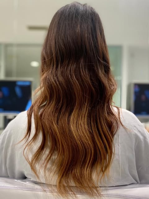 Capelli castani lunghi visti di spalle: balayage ramato che schiarisce progressivamente dalle radici scure alle punte, onde ampie.